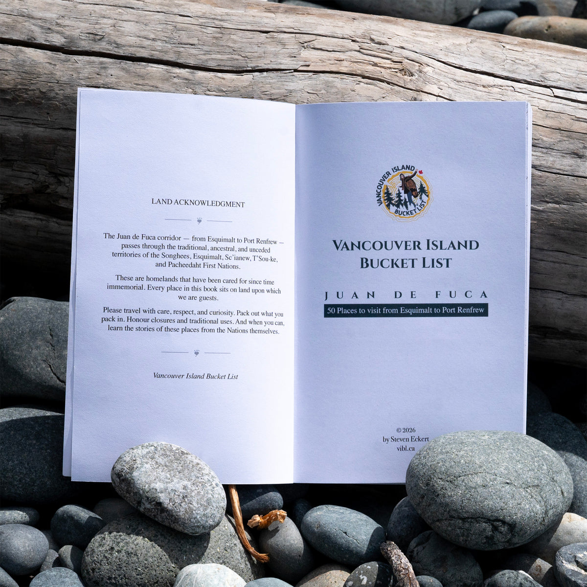 An open printed booklet titled 'Vancouver Island Bucket List' lies on smooth gray rocks against a weathered wood background. The pages are white with black text and a small multicolor island illustration at the top right.